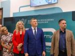 На фото группа людей в деловой одежде стоит на фоне баннера Министерства просвещения Российской Федерации, над ними — экран с иллюстрациями.
