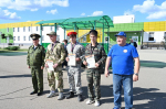 На фото — группа юношей в камуфляжной форме с грамотами и медалями, слева — военнослужащий в форме, справа — мужчина в синей футболке и кепке; на фоне — здание с жёлто‑зелёной отделкой и навес с зелёной кровлей.
