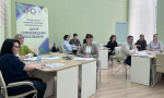 В помещении «Центра сопровождения образования» Краснодарского края группа специалистов участвует в рабочем совещании, сидя за столами с документами и канцелярскими принадлежностями.