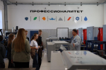 На фото — учебная мастерская в рамках проекта «Профессионалитет»: преподаватель объясняет материал группе обучающихся на фоне станков и тематической надписи на стене.